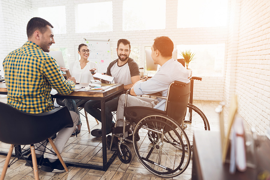 Disability Insurance - Man in a Wheelchair Communicates with Fellow Employees at the Office during a Business Meeting